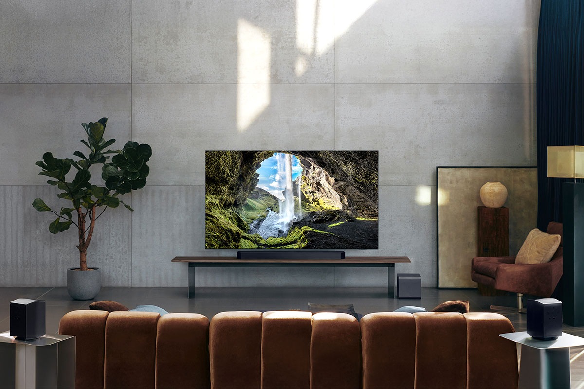 Q990F soundbar placed below TV and subwoofer in living room. Two rear speakers placed on side tables behind the sofa.