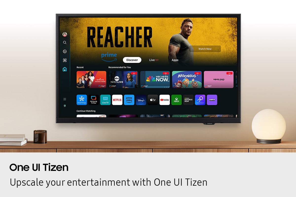 A wall-mounted Samsung TV displays popular apps and curated content on the One UI Tizen home screen.