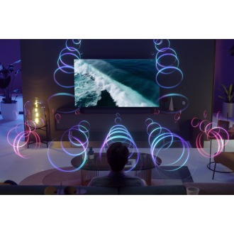 A person is sitting in front of a QLED TV as sound waves fill the room with 3D surround sound.