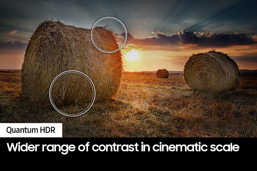 The sun is setting over a wide field with emphasis on a large hay stack.