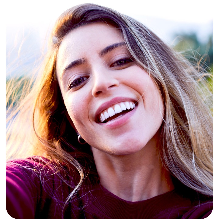 A woman looking into the camera, taking a selfie. The background is subtly blurred out with the bokeh effect.
