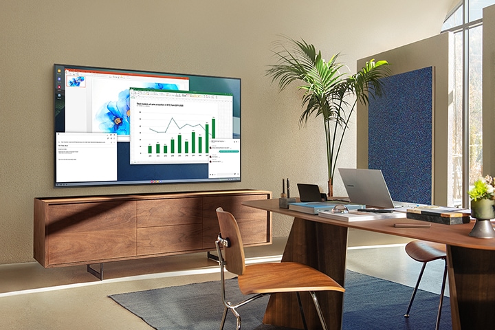 In a living room home office, A TV screen shows PC on TV feature which allows home TV to connect to office PC.