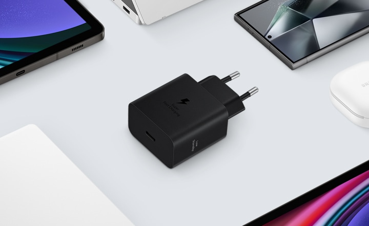 A top view of various Samsung Galaxy devices are shown with a black Power Adapter placed at the center. To the left, a Galaxy Book3, to the right Galaxy Buds2 Pro in White, a Galaxy Tab S9 and Galaxy S24 Ultra are also shown.