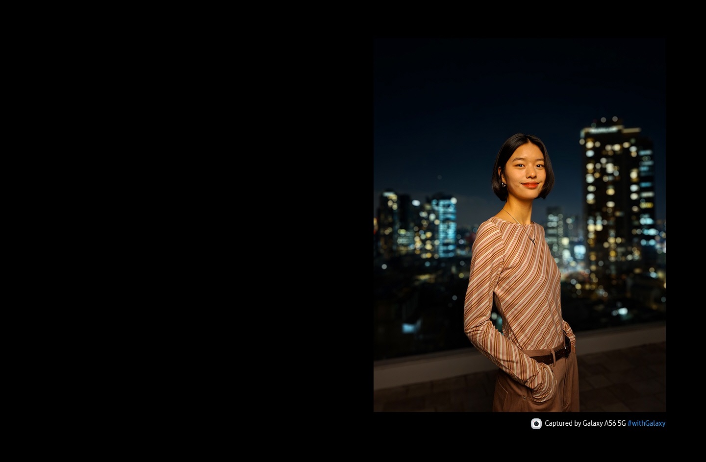 Person smiling into the camera. Night view of a city in the background. At the bottom is camera icon with text Captured by Galaxy A56 5G hashtag with Galaxy.