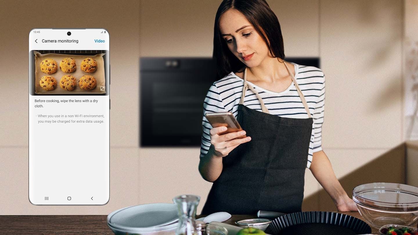 Arată o femeie în fața unui cuptor privindu-și smartphone-ul. Un prim plan al ecranului telefonului arată funcția de monitorizare a camerei a aplicației SmartThings, care afișează un videoclip în timp real cu cookie-uri coapte în cuptor.