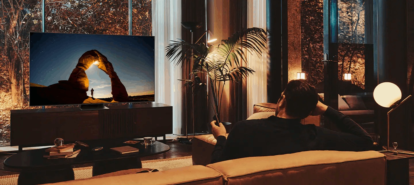 Telewizor Samsung Neo QLED 8K Excellence Line QN800B na szafce naprzeciwko mężczyzny siedzącego na kanapie
