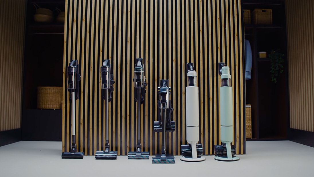 Sześć modeli odkurzaczy bezprzewodowych Samsung - Jet 65, Jet 75, Jet 85, Jet 95, Bespoke AI Jet Lite oraz Ultra przy drewnianej ścianie.