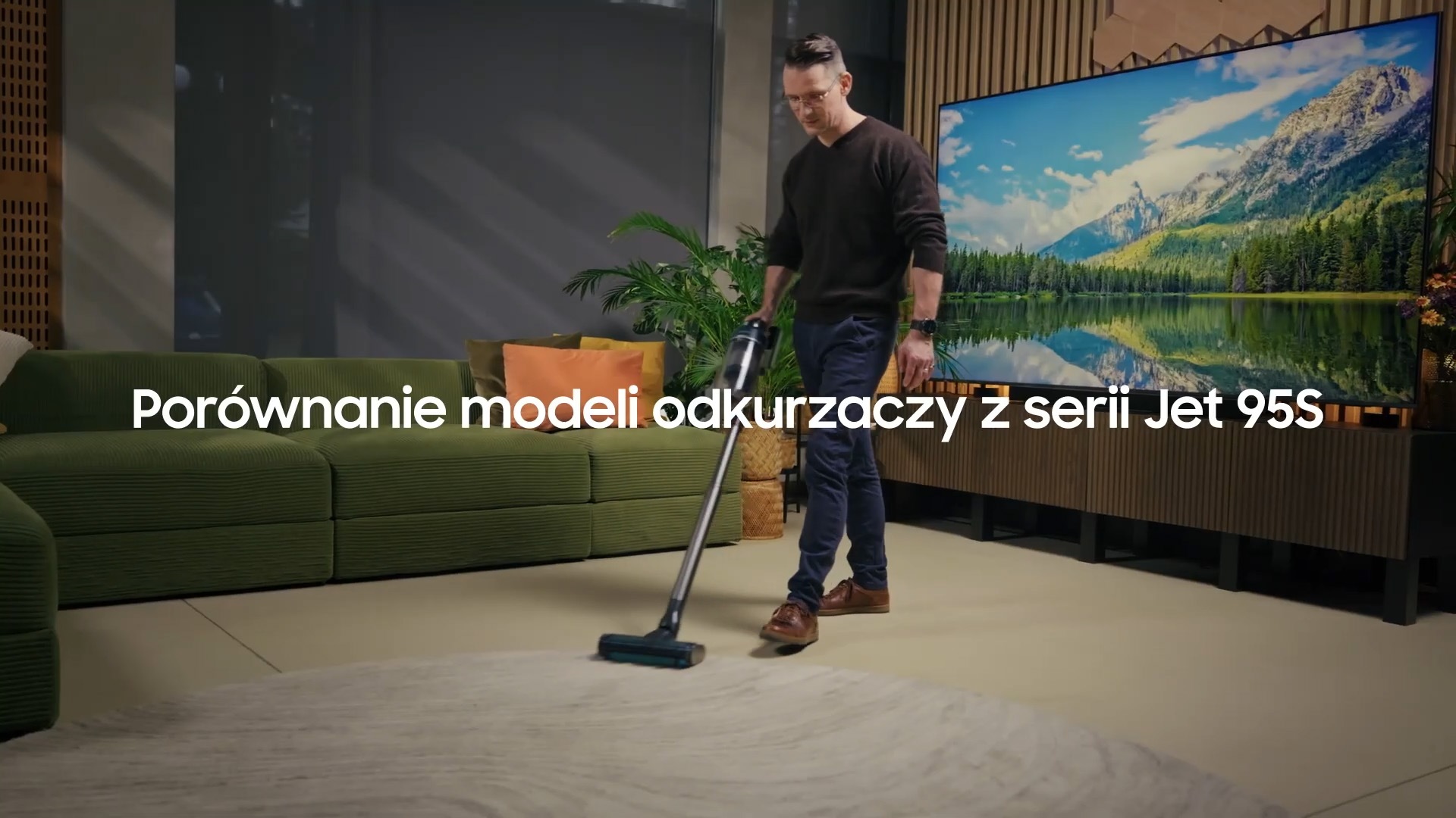 Mężczyzna odkurza salon odkurzaczem Samsung Jet 95S. W salonie znajduje się zielona kanapa i nowoczesny telewizor Samsung.