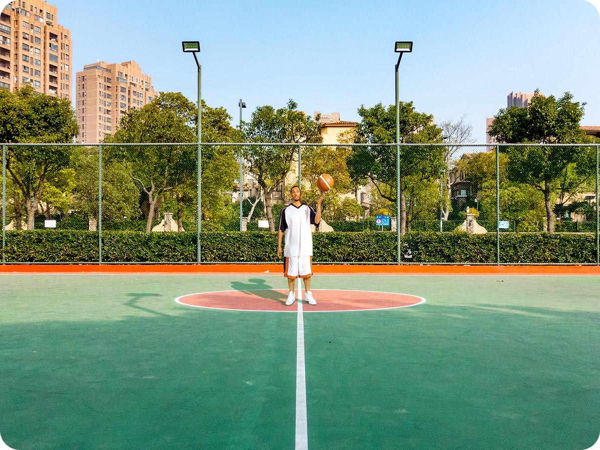 A man standing in a basketball court. Taken on the Ultra Wide Camera, you can see more of the court and scene around him.
