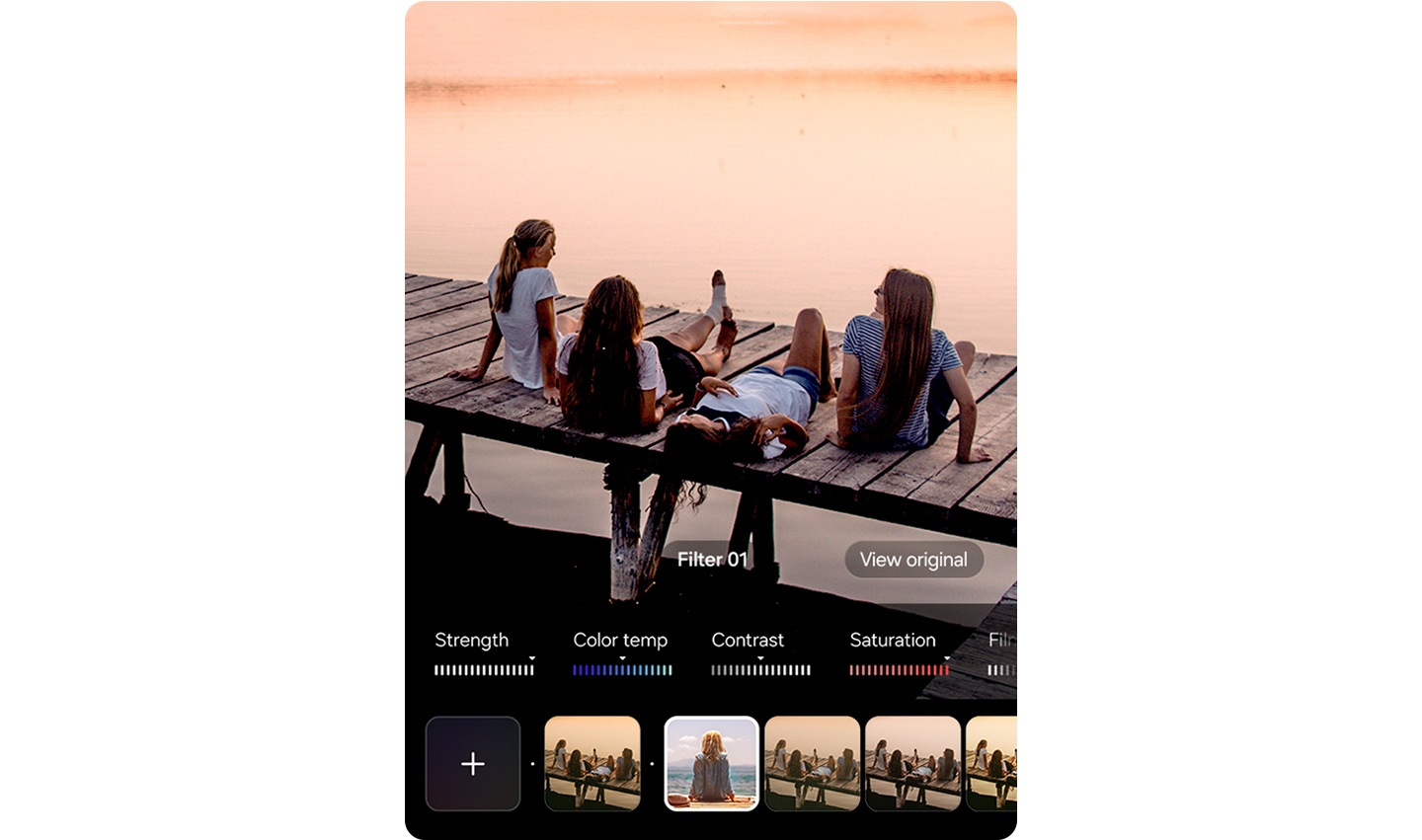 Four people sit on a wooden dock by a body of water during sunset. An editing interface is visible at the bottom with sliders for strength, color temperature, contrast and saturation, along with filter options, one of which is selected in the center.