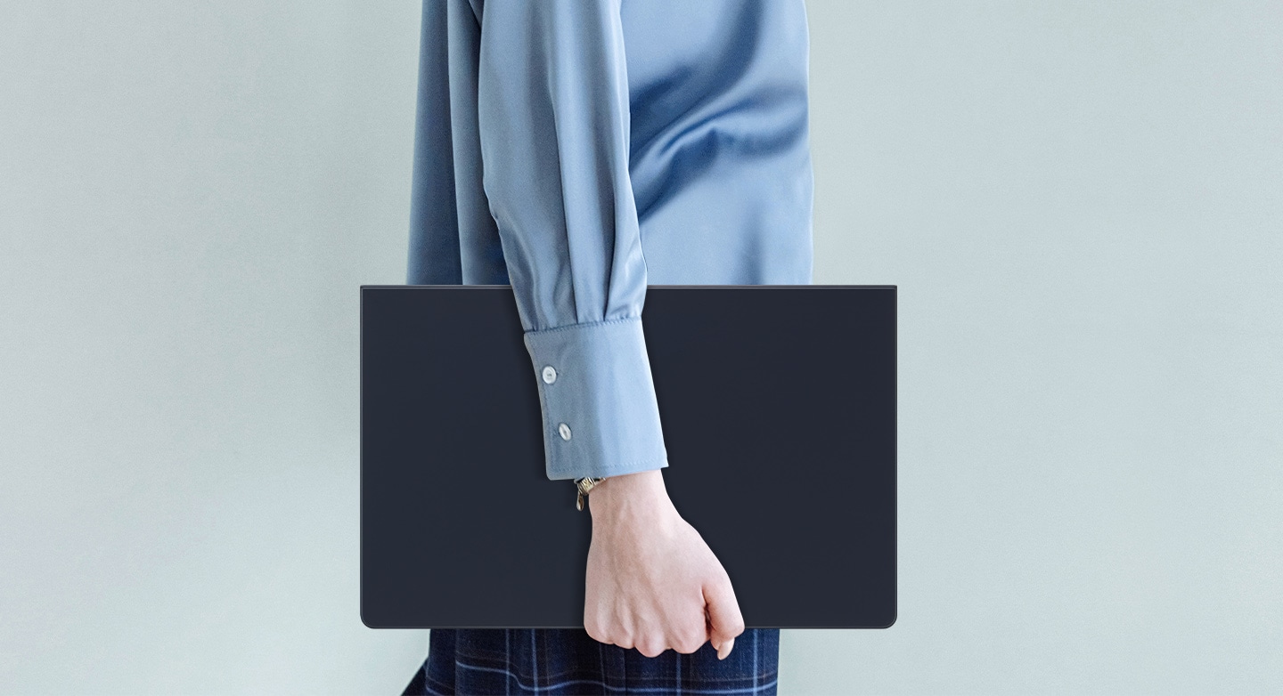 Человек в синей рубашке идёт, держа в руках Galaxy Tab S9 Ultra в чехле-клавиатуре Book Cover Keyboard Slim.