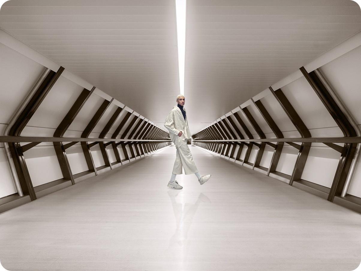 A man standing in a corridor, and with the Ultra Wide Camera, much more corridor can be taken in the shot.