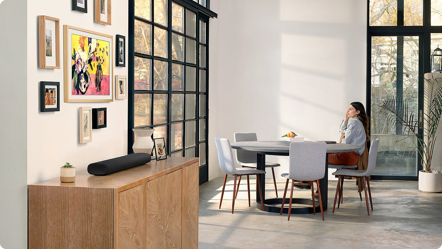 All-in-one design of S60A soundbar blends elegantly with living room interior as a woman sits at the table and looks out the window.