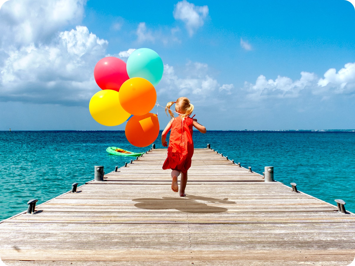 A girl is running on a dock holding a bundle of balloons.