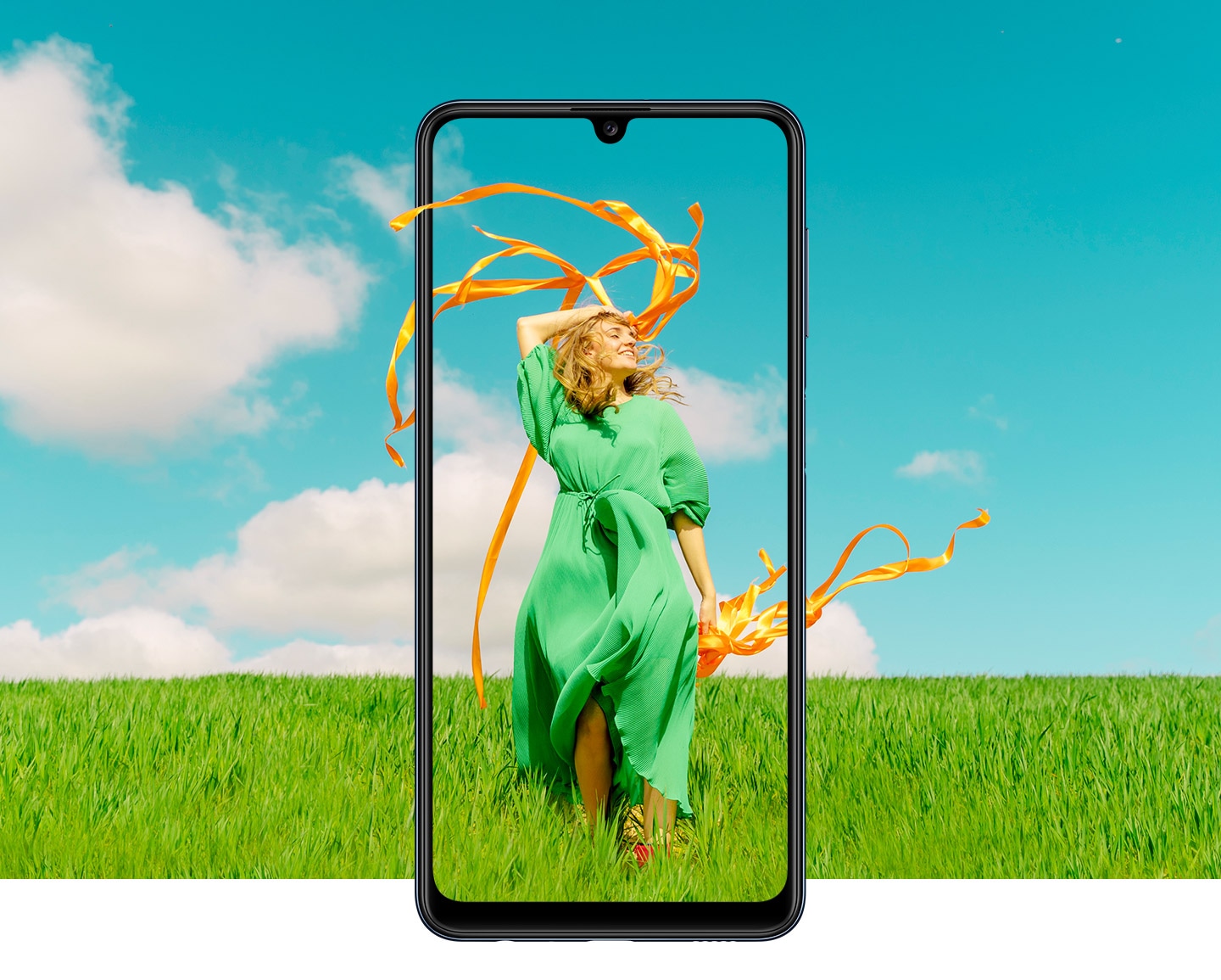 A Galaxy M32 is seen from the front. Onscreen, a woman in a green dress is dancing as ribbons in her hands flow in the breeze. The ribbons and green field background go beyond the bezel.