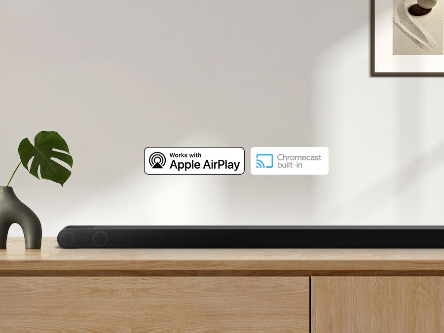 Логотип Apple AirPlay, встроенный логотип Chromecast и логотип Ok Google можно увидеть вместе со звуковой панелью Samsung S800B, которая находится на шкафу в гостиной.
