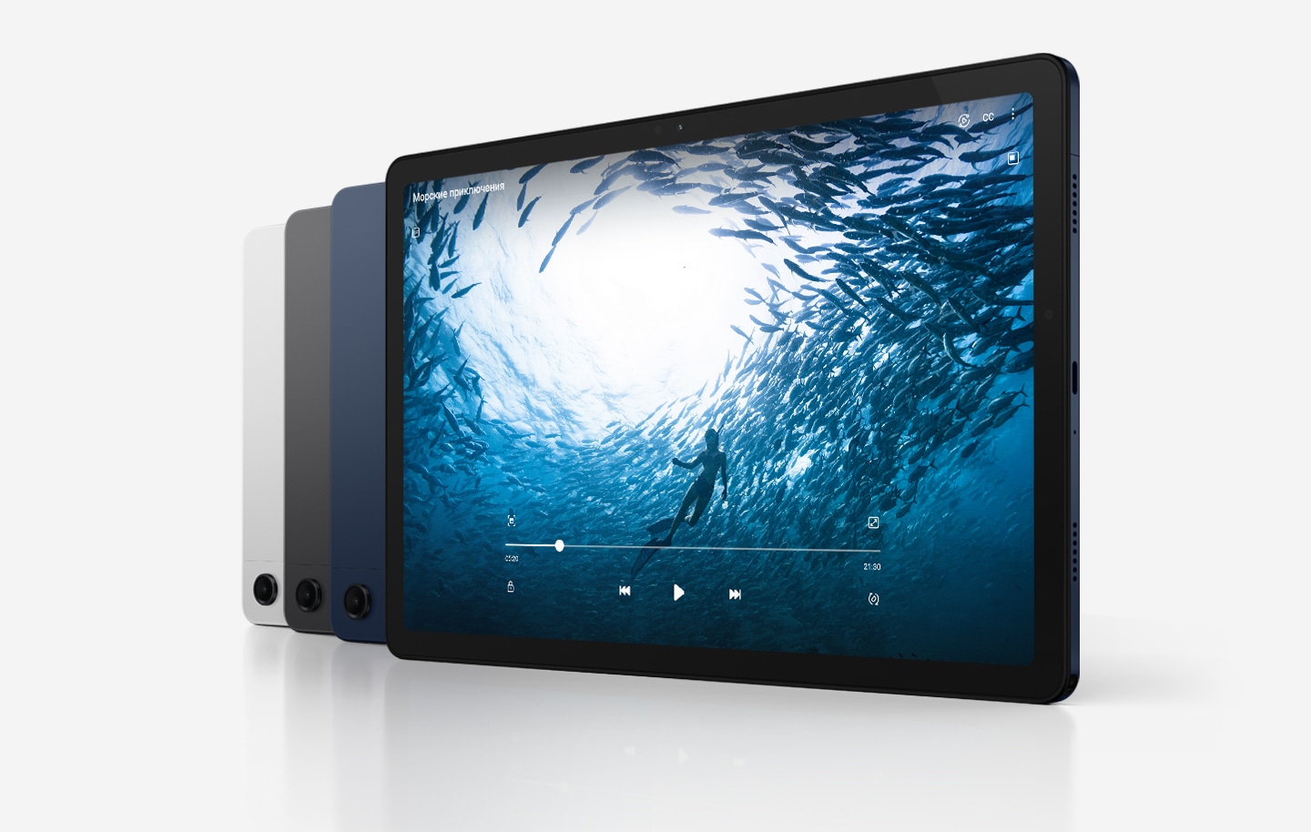 Четыре планшета Galaxy Tab A9+ расположены по диагонали. Три устройства обращены к зрителю задней панелью, а планшет на переднем плане показан со стороны экрана. Цвета устройств слева направо:  "Серебристый" и "Графитовый", а остальные - "Темно-синие". На экране устройства справа окно с видео под названием Морские приключения, в котором виден человек, плывущих в океане в окружении рыб.