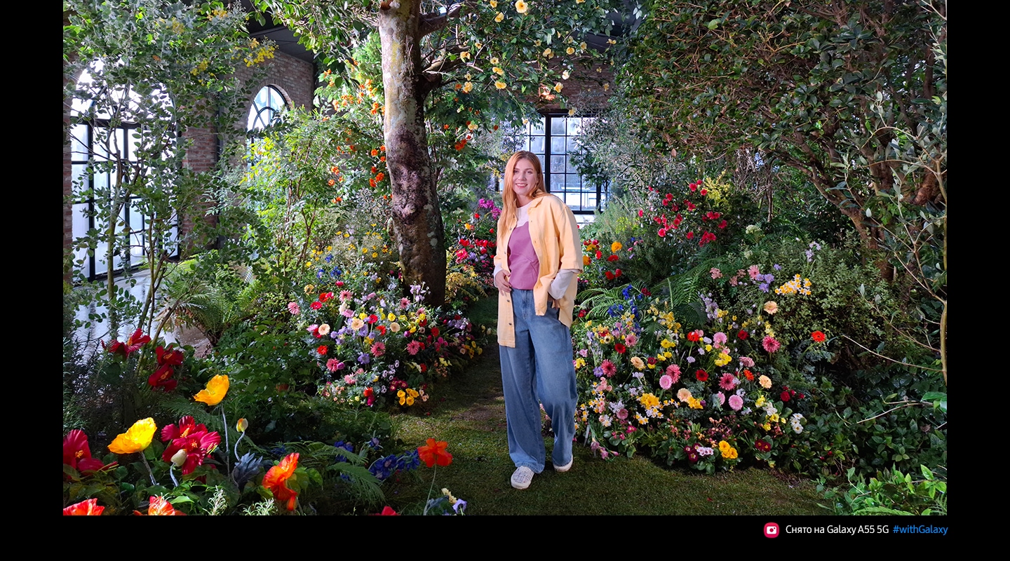Фотография, сделанная 50 МП камерой высокого разрешения, на которой изображен человек, стоящий в роскошном внутреннем саду, полном ярких цветов и зелени. Текст: Снято камерой телефона Galaxy  A55 5G #withGalaxy.