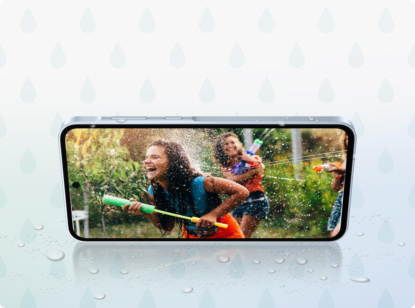  Смартфон в альбомной ориентации с изображением двух девушек, играющих в воде. Телефон в окружении капель воды.
