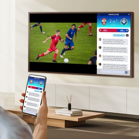 Человек одновременно смотрит на два разных экрана телевизора. У них есть один экран, на котором отображается футбольный матч, и второй экран, на котором отображается их мобильный телефон и статистика в реальном времени.