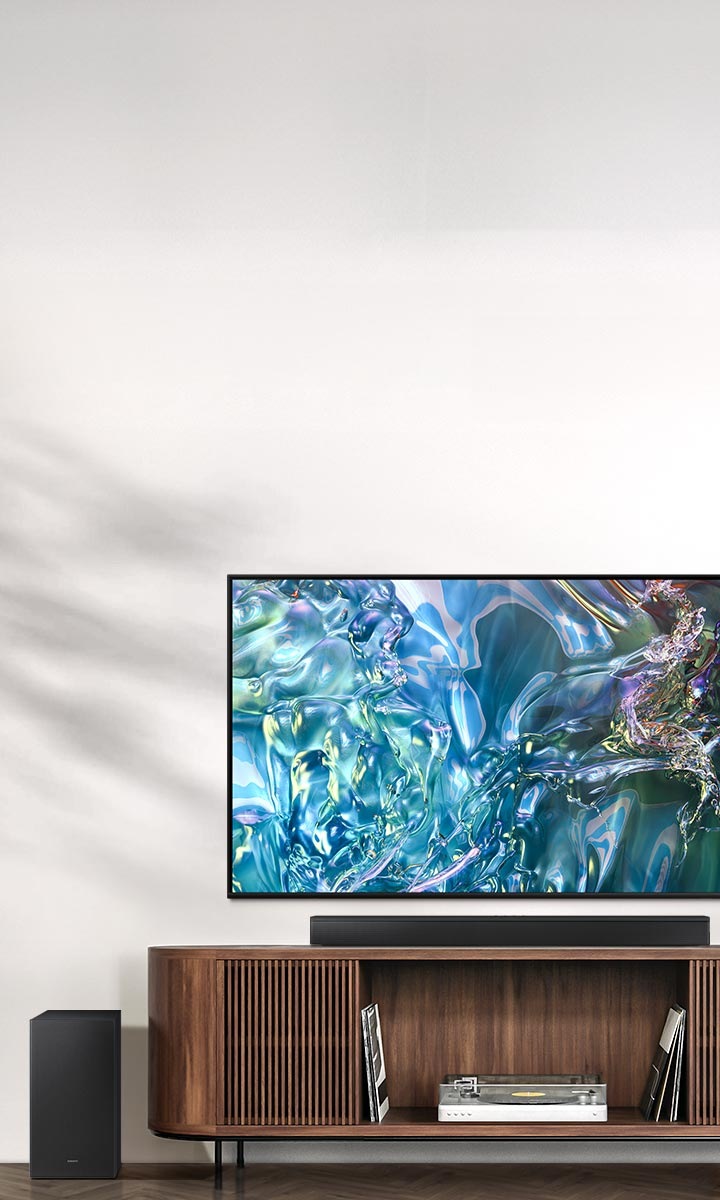 На экране телевизора отображается синяя волна. Внизу находится подставка под телевизор со звуковой панелью сверху и сабвуфером сбоку.