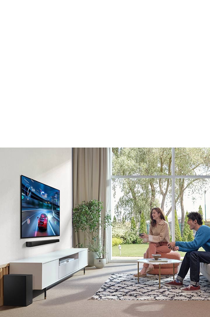 Мужчина и женщина играют в гоночную игру на своем телевизоре, а звуковая панель под ним обеспечивает оптимизированный звук в игровом режиме.