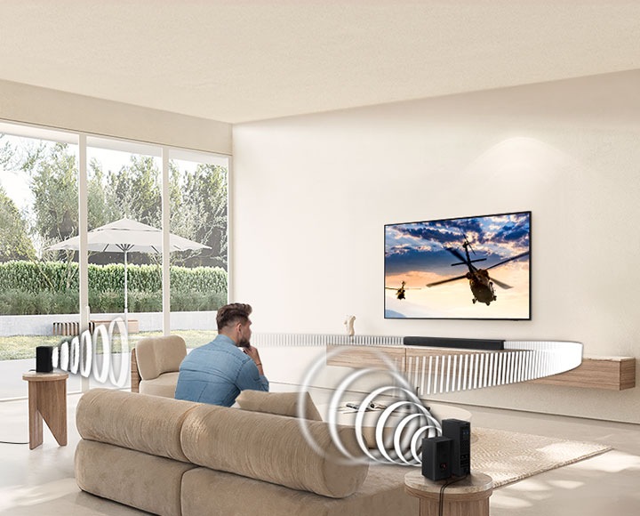 Мужчина смотрит телевизор. Саундбар и задние динамики излучают звуковые волны разных типов, направляющиеся в сторону человека.