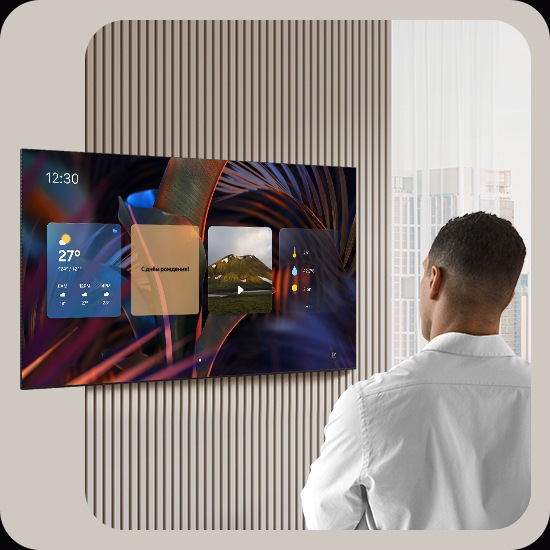 Мужчина смотрит на пустой экран телевизора. Экран включается и отображает Daily Board, который переключает виджеты для погоды, заметок, музыки, домашней статистики, Samsung TV Plus и советов. Он также отображает время и дату, а также голосовое сообщение с предложением включить расслабляющую музыку.