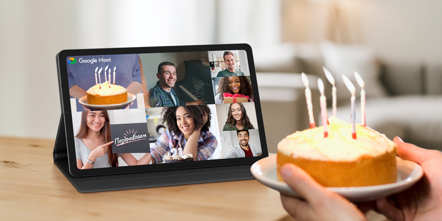 Человек держит торт с зажженными свечами перед устройством Galaxy Tab S6 Lite, закрепленным в альбомной ориентации с помощью чехла-обложки Book Cover. Экран устройства разделен на прямоугольные изображения, чтобы показать, что несколько человек находятся на связи посредством видеозвонка. На одном изображении показан торт с зажженными свечами, а на каждом из других изображений изображен улыбающийся человек. Логотип Google Meet отображается в верхней левой части экрана. 