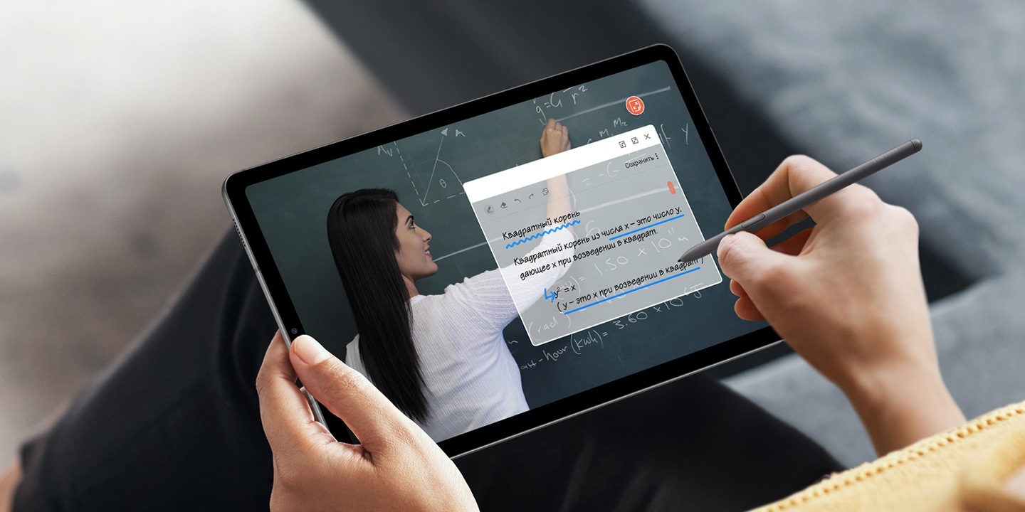 Человек держит в руках устройство Galaxy Tab S6 Lite в альбомной ориентации, на экране отображается полноэкранная видеолекция женщины, пишущей на доске. Человек делает заметки с помощью пера S Pen в полупрозрачном окне приложения Samsung Notes, наложенном на видеолекцию.