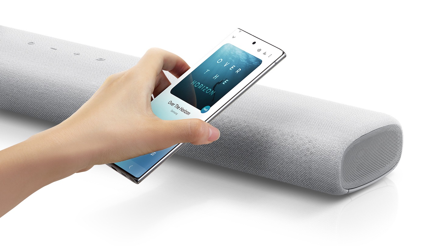 A hand taps a smartphone with the Samsung music app on-screen on the soundbar and the soundbar instantly plays music, showing how easy it is to switch from smartphone to soundbar.