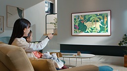 Мать и ребенок сидят на диване и смотрят на детские рисунки, показанные на The Frame TV.