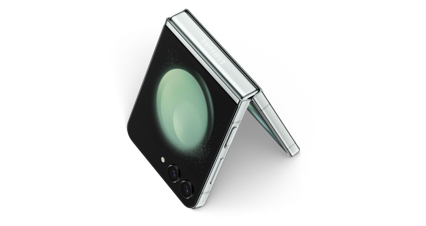 An extreme closeup of a folded Galaxy Z Flip5 seen from the Flex Window and bottom frame. Zooming out, the device opens to stand like a tent.