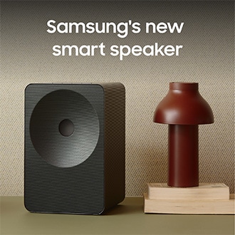 Music Studio 7 på ett bord med en lampa som står ovanpå två böcker. En text som säger "Samsungs nya smarta högtalare".