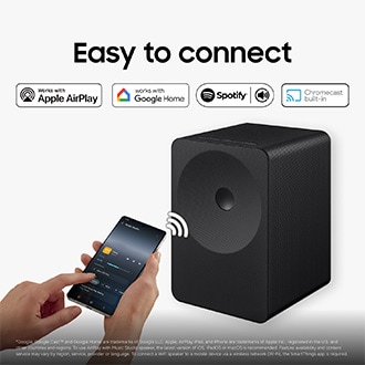 En person använder en smartphone för att trådlöst streama musik till Music Studio 7-högtalaren på ett skrivbord, vilket visar enkel Wi-Fi- och Bluetooth-anslutning för sömlös musikuppspelning.