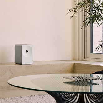 Music Studio 7-högtalare med beige hyllplan. Högtalaren står bland dekorationer och en växt, vilket skapar en varm och mysig atmosfär i ett modernt vardagsrum.
