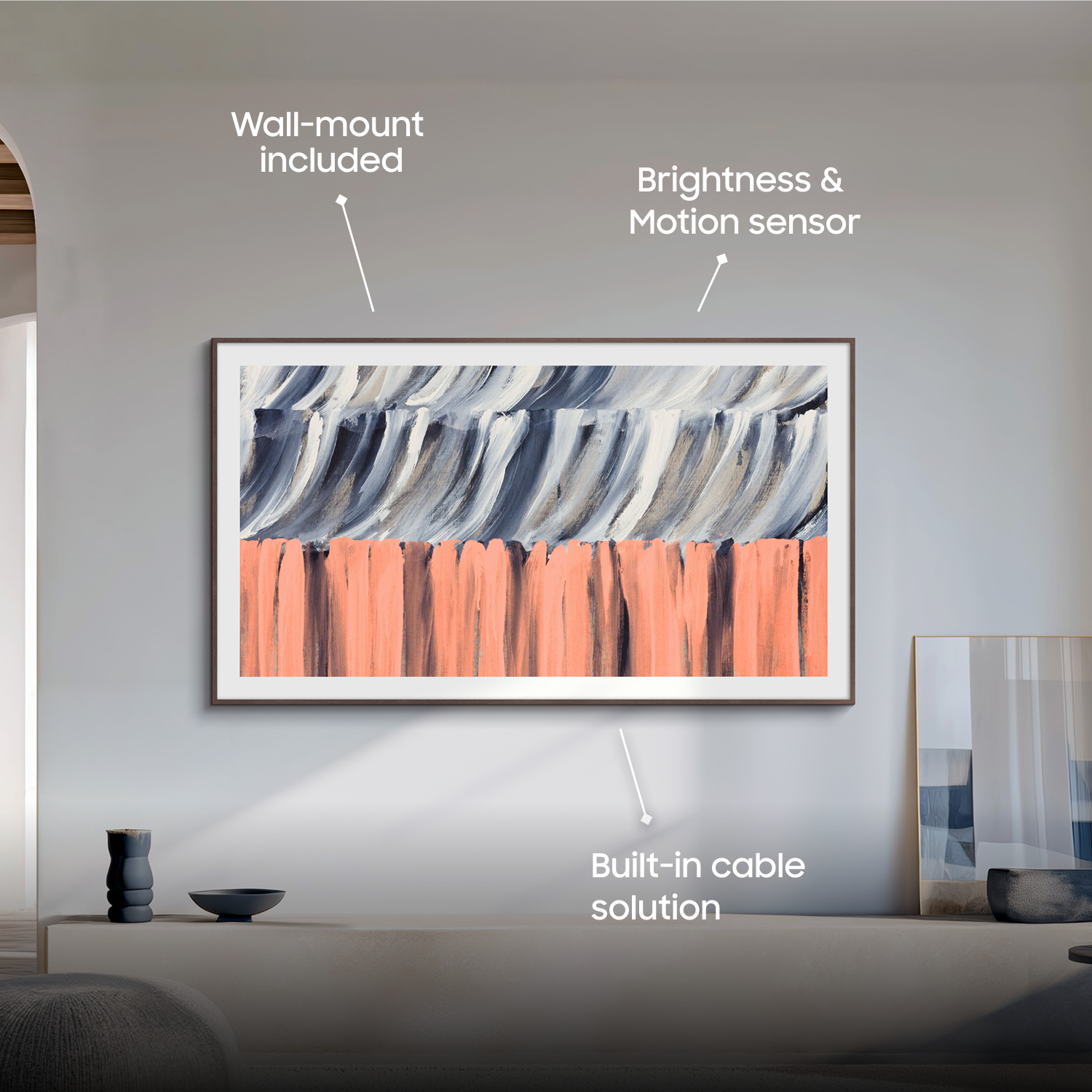 The Frame is mounted on a wall in a living room. Text that says "Wall-mount included," "Brightness & motion sensor," and "Clutter-free setup with Wireless One Connect."