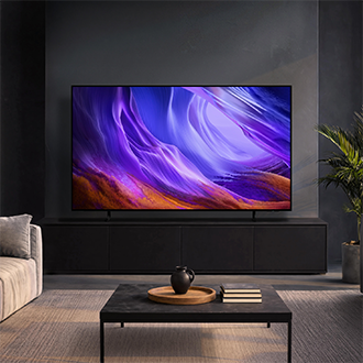 Samsung OLED‑TV i ett mörkt, modernt vardagsrum som visar livfulla lila abstrakta bilder som kompletterar den eleganta inredningen.