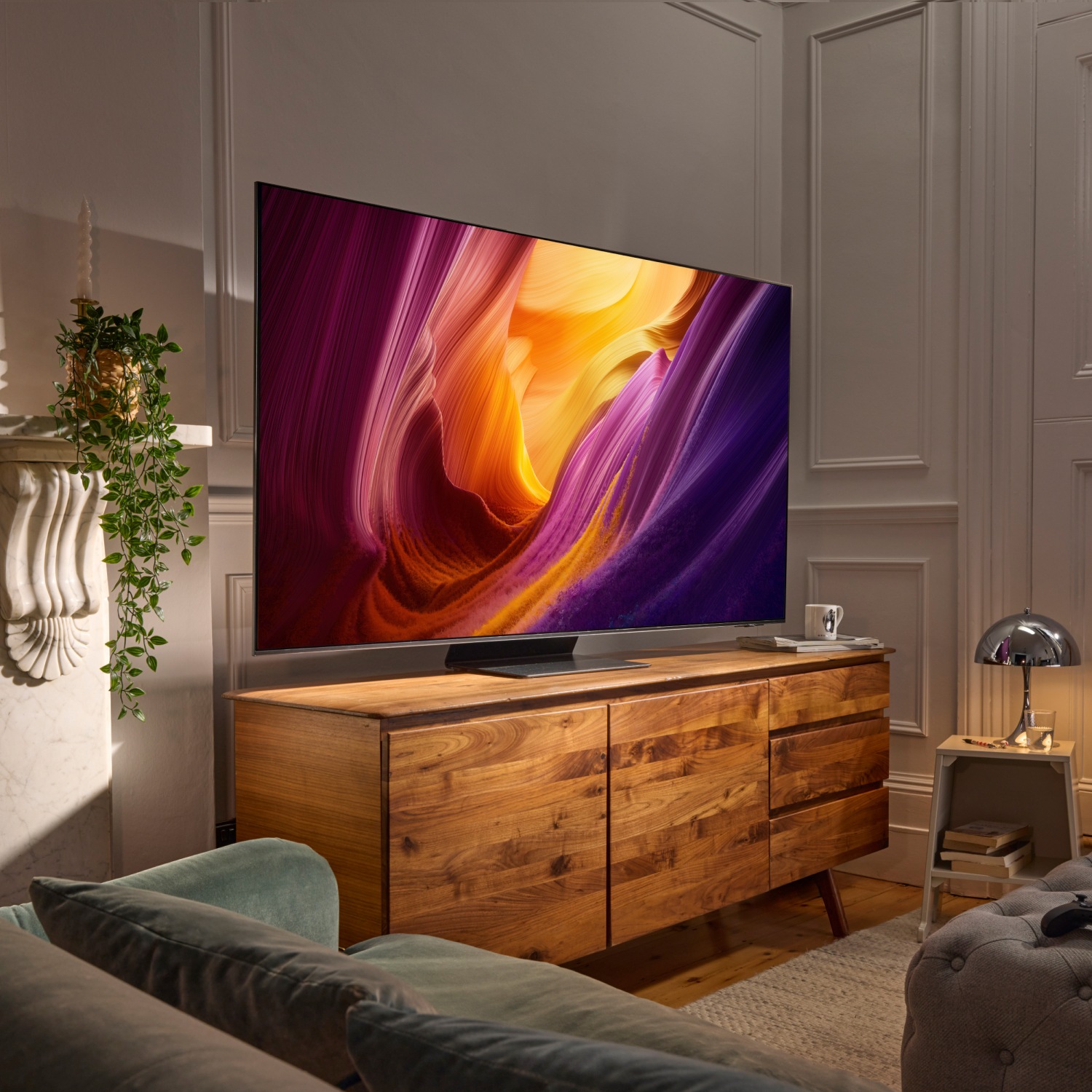 TV som visar livfulla canyon‑färger, monterad ovanför en träkonsol i ett ombonat vardagsrum med grön soffa och växter.