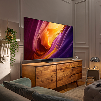 TV som visar livfulla canyon‑färger, monterad ovanför en träkonsol i ett ombonat vardagsrum med grön soffa och växter.