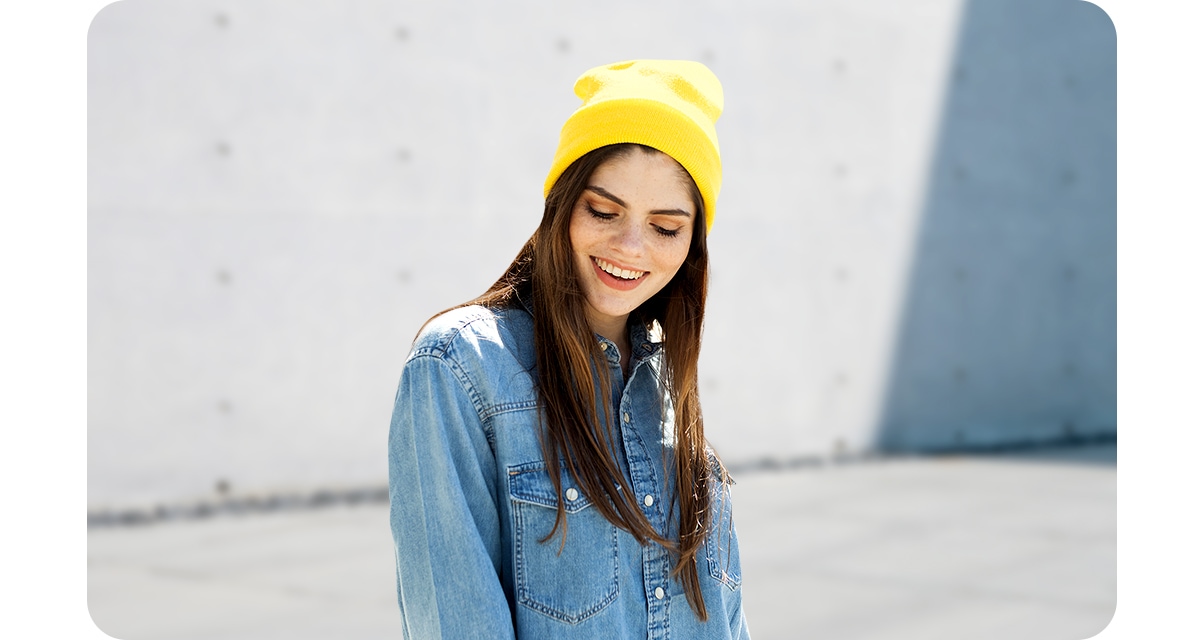 Samsung Galaxy M32 camera taking high quality portrait shot of a young, long-haired woman looking down, with the gray surface of the walls blurred out in the background.