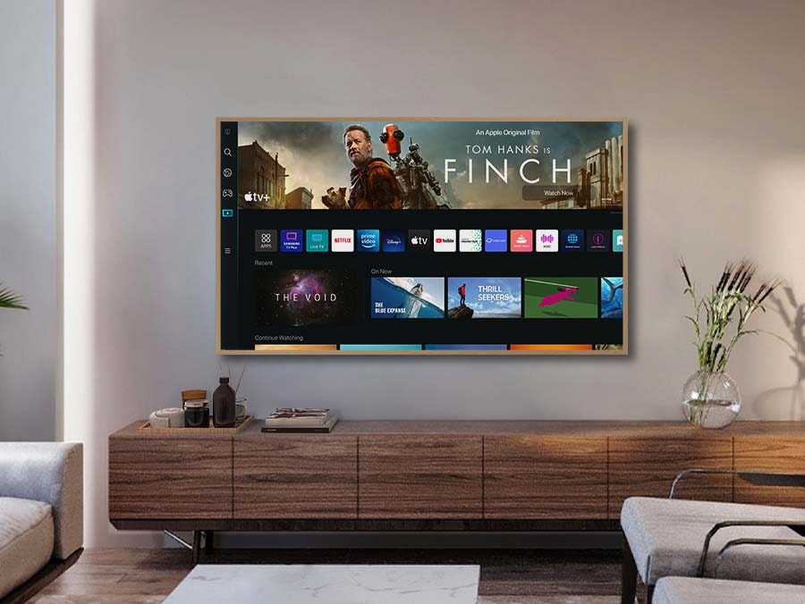 A girl is pointing the remote towards The Frame, which shows the Smart Hub home screen.
