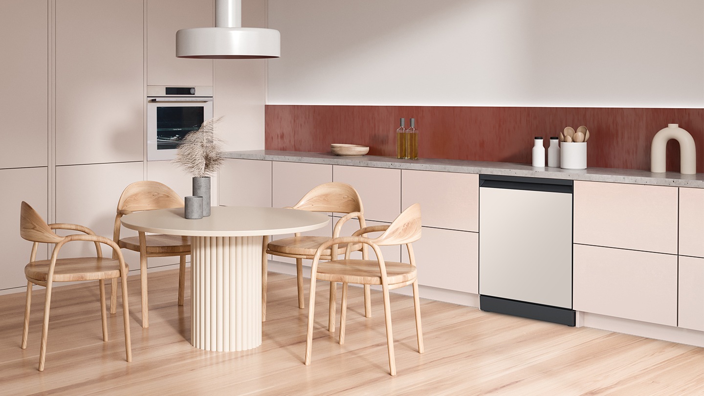 Shows the dishwasher with a white door panel that complements the pale pink and natural wood colored design of the kitchen cabinets, table and chairs and flooring.