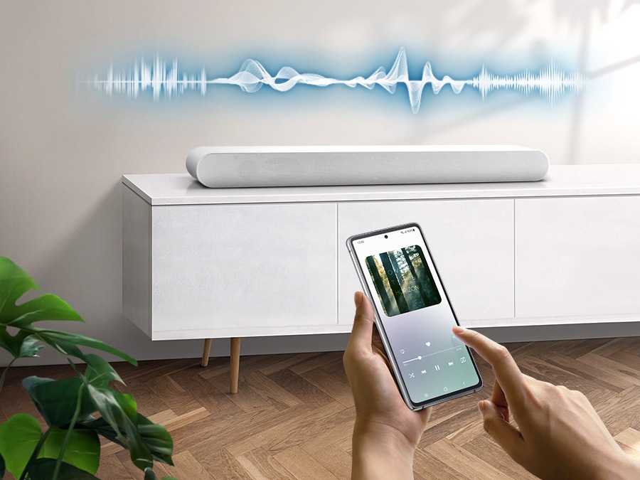 User plays music on their smartphone directly from their soundbar, which has soundwave graphics above it, using Music Mode which allows easy smartphone connectivity so optimized sound can be heard from soundbar.