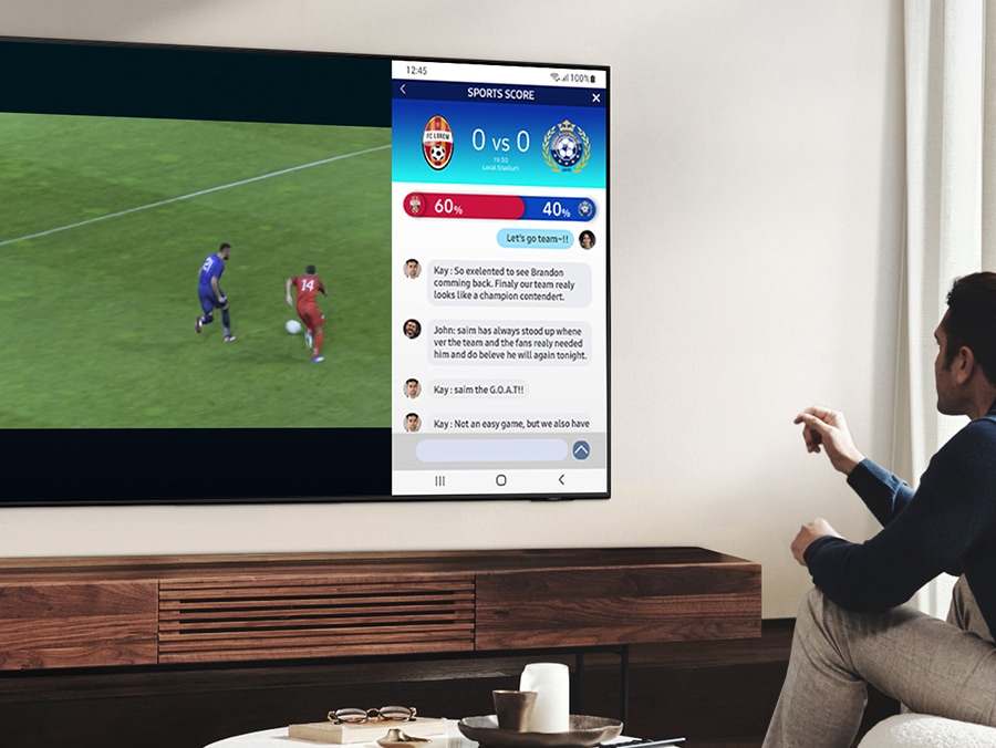 A man is watching a soccer game on his TV simultaneously reading the news on the same screen.