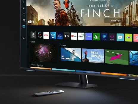 The monitor screen shows a variety of content apps and individual content choices in a card format. A remote controller rests next to the monitor.