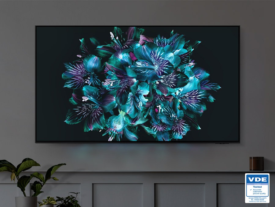 A TV is displaying a colorful flower-like pattern on its screen. The color details of the flower are very vivid. VDE 01/2024 Tested Accurate calibrated picture quality www.VDEiinfo.com ID. 40057839 Tested by VDE Germany.