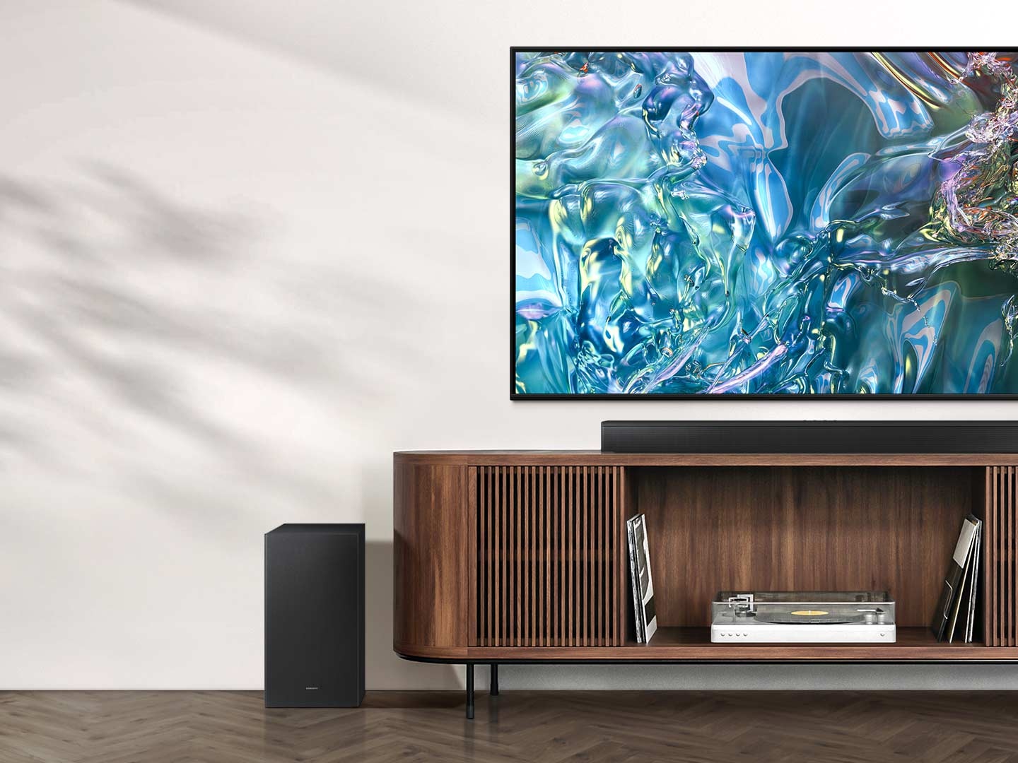 A TV shows a blue wave pattern on its screen. Underneath is a TV stand with a Soundbar on top and a subwoofer to the side.