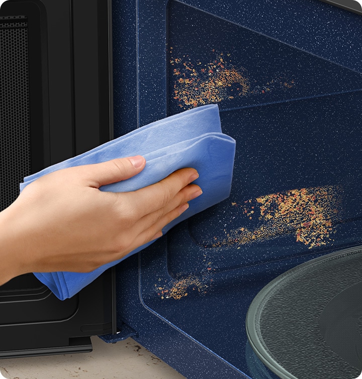 A person cleans up the surface of the microwave oven with a simple swipe with a cloth.