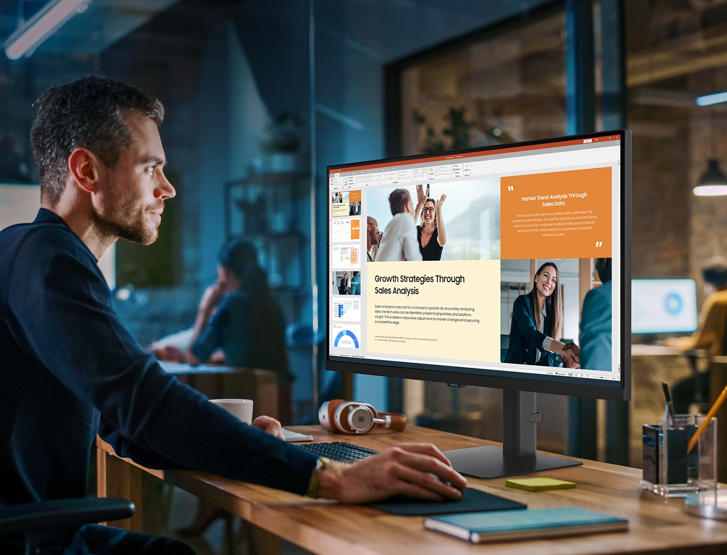 A man works at a desk, using a mouse. The monitor shows powerpoint. Above him, text reads "Expand your creative realm"